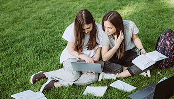 Students looking at laptop and books on campus grounds